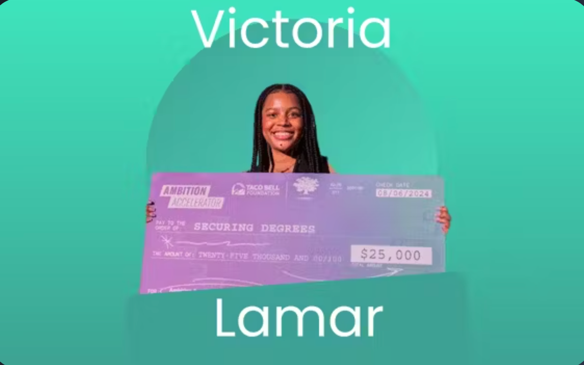 A smiling woman holds a large purple check for $25,000. The check is from Ambition Accelerator and the Taco Bell Foundation. The name Victoria Lamar appears above and below her on a green background.